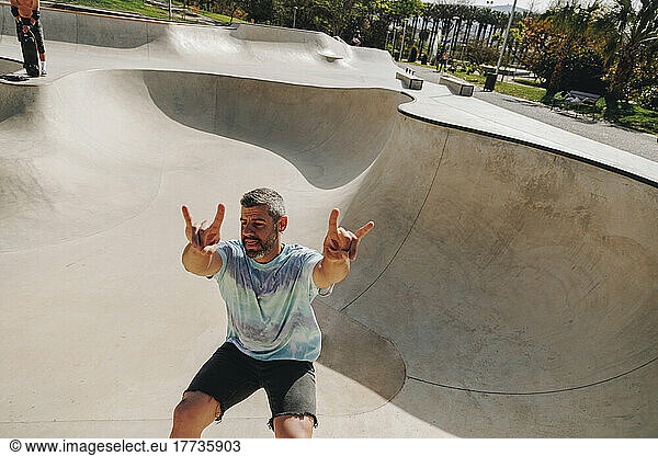 Man showing horn sign and skateboarding on sports ramp