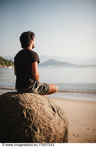 Man siting on a rock meditating on the beach