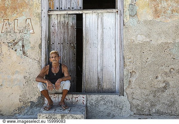 Man sitting at the doorstep of his house with a decayed fa?ade of crumbling plaster and a weathered wooden door. Manzanillo  Cuba.