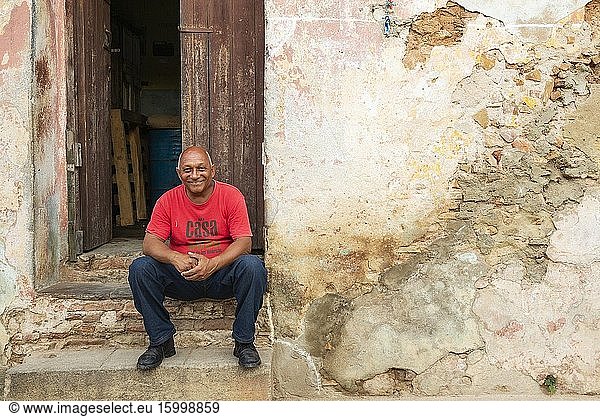 Man sitting at the doorstep of his house with a decayed fa?ade of crumbling plaster. Trinidad  Cuba.