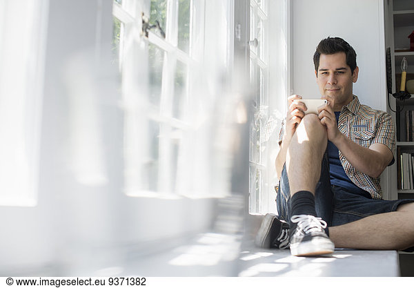 Man sitting by a window  holding a cell phone.