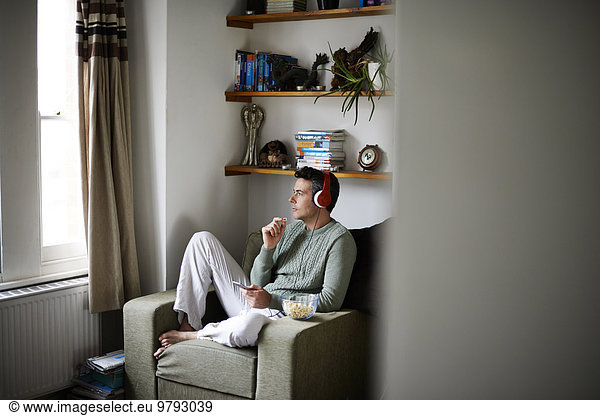 Man sitting in armchair with headphones looking through window