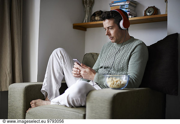 Man sitting in armchair with headphones using smartphone