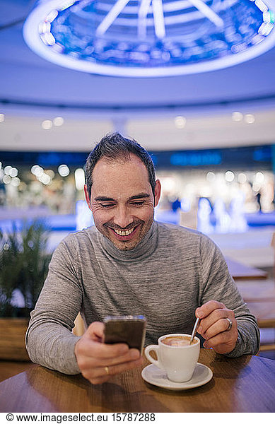 Man sitting in cafeteria  drinking coffee  using smartphone