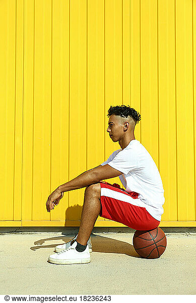 Man sitting on basketball in front of yellow wall