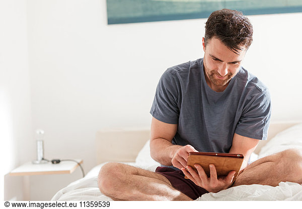 Man sitting on bed using digital tablet