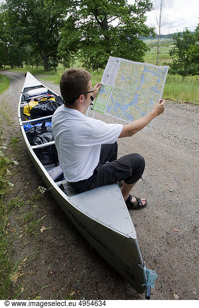 Man sitting on canoe and looking at map