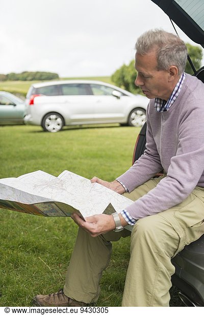 Man sitting on car boot reading map