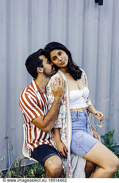 Man sitting on chair kissing girlfriend outside house