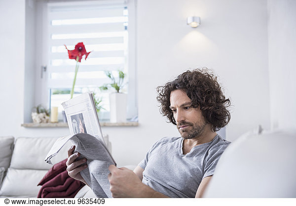Man sitting on couch and reading a newspaper