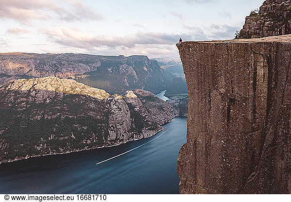 Man sitting on edge of cliff at fjords in Prekeistolen Norway