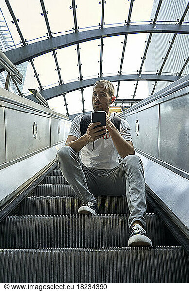 Man sitting on escalator with smart phone