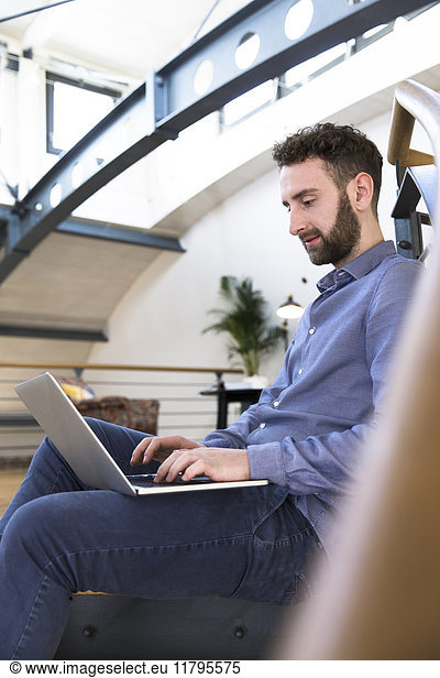 Man sitting on floor using laptop in modern office