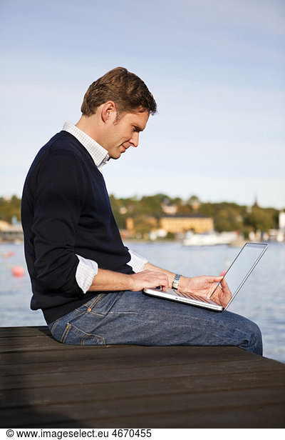 Man sitting on jetty with computer