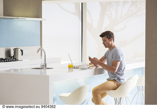 Man sitting on stool at kitchen island and using phone