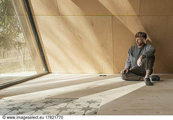 Man sitting on the floor in wooden eco house looking out of window