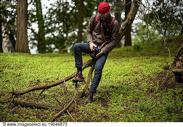 Man sitting on tree holding camera looking at hiking boots