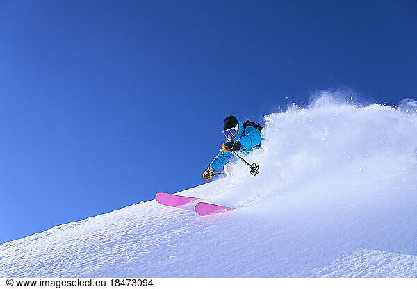 Man skiing downhill on snow under blue sky