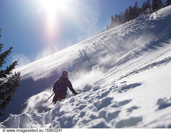 Man skiing in powder backlit by sun