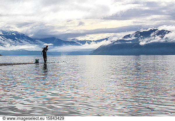 Man skipping rock in New Zealand with mountains in the background.