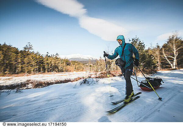 Man skis on snow covered trail towing sled  Katahdin  Maine