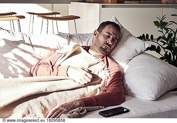 Man sleeping by smart phone on sofa at home