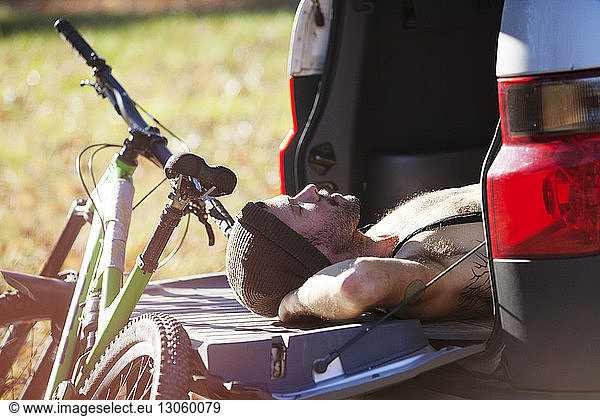 Man sleeping in car trunk by mountain bike during sunny day
