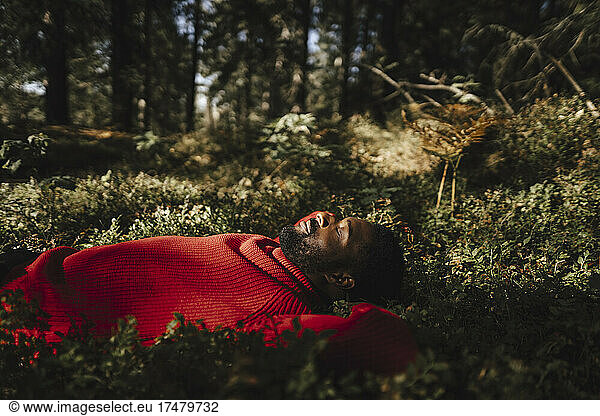 Man sleeping while relaxing on plants in forest