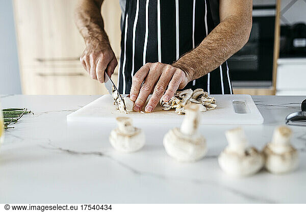 Man slicing mushroom in kitchen at home