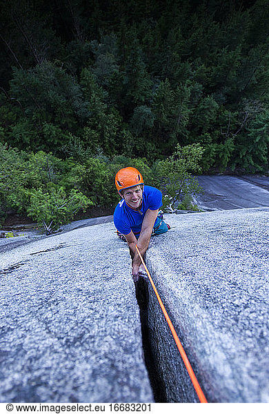 Man smiling and looking up at camera while climbing off width Squamish
