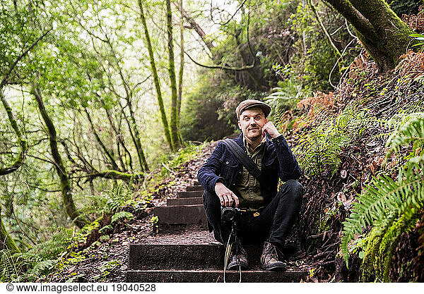 Man smiling at camera and sitting on wooden steps in forest