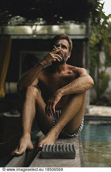 Man smokes a cigarette in a private villa by the pool.