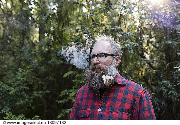 Man smoking pipe while standing against trees
