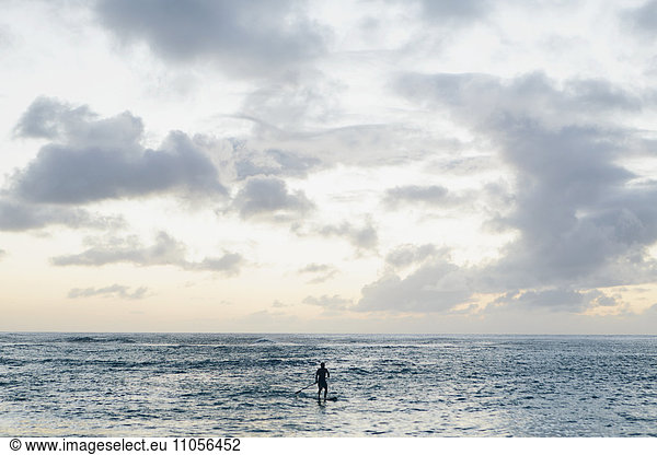 Man stand up paddling in calm waters at dusk