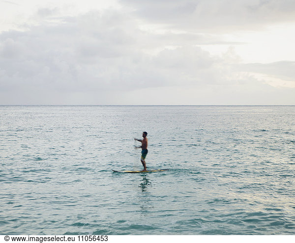 Man stand up paddling in calm waters at dusk