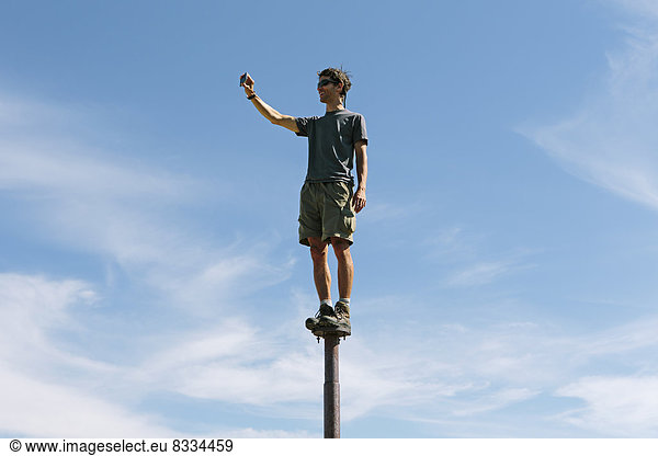 Man standing and balancing on a metal post  looking towards expansive sky  on Surprise Mountain  Alpine Lakes Wilderness  Mt. Baker-Snoqualmie national forest.
