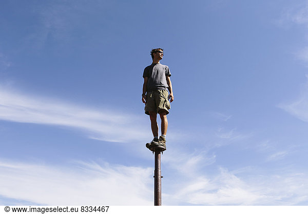 Man standing and balancing on a metal post  looking towards expansive sky  Surprise Mountain  Alpine Lakes Wilderness  Mt. Baker-Snoqualmie National forest.