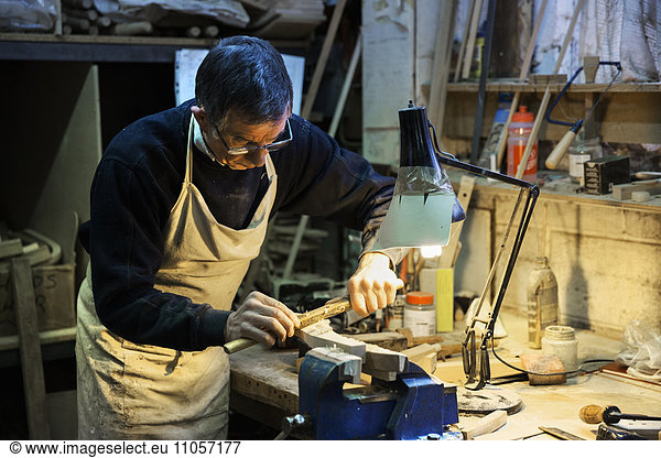 Man standing at a work bench in a carpentry workshop  working on a piece of wood secured in a bench vice with a spokeshave.