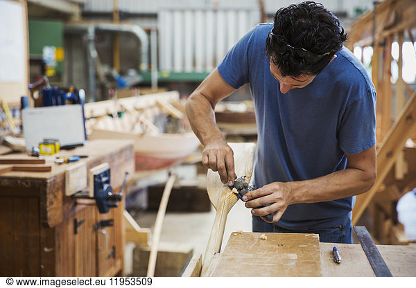 Man standing in a boat-builder's workshop  working on a wooden oar.