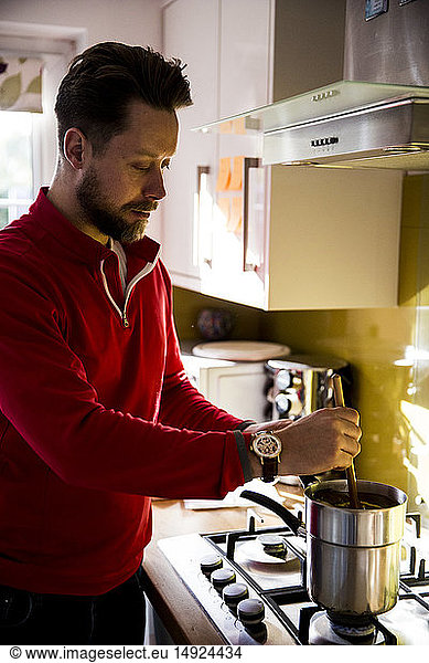 Man standing in a domestic kitchen  making jar candles.