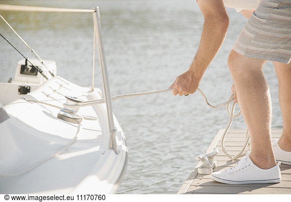 Man standing on a jetty  towing a sail boat.