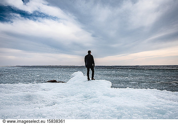 Man standing on an icy shoreline of a lake looking into the distance.