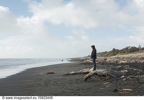 Man standing on driftwood looking at the ocean