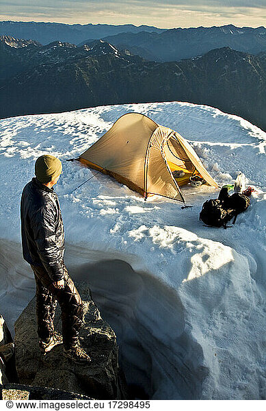 Man standing on mountain summit  looking out at tent and scenic view