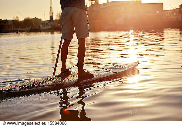 Man standing on paddleboard on river at dawn  shot from behind