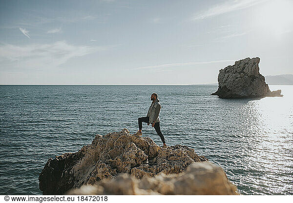 Man standing on rock in front of sea at sunset