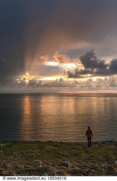 Man standing watching sunrise on mountainous seacoast