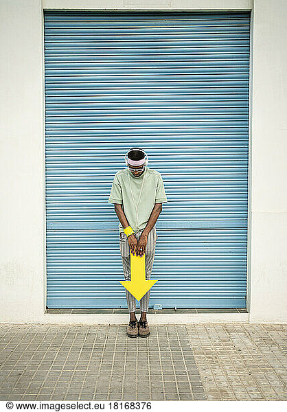 Man standing with arrow sign looking down in front of closed blue shutter