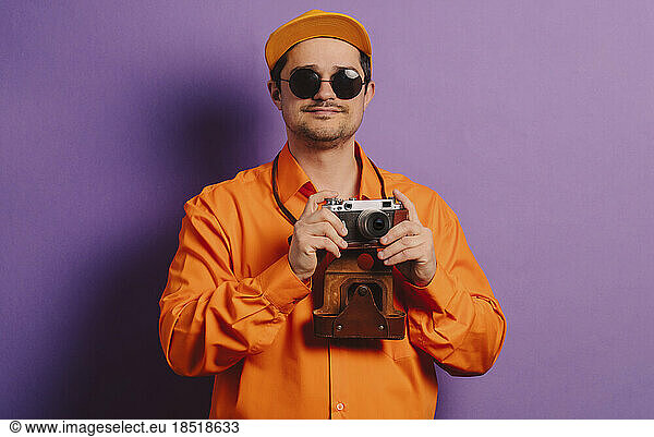 Man standing with retro style camera against purple background