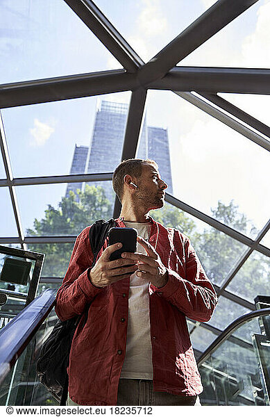 Man standing with smart phone on escalator